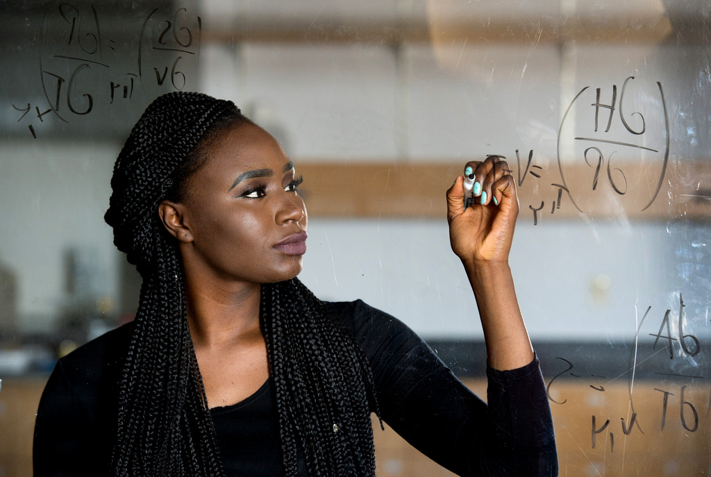 An African American female student completing equations on a whiteboard.