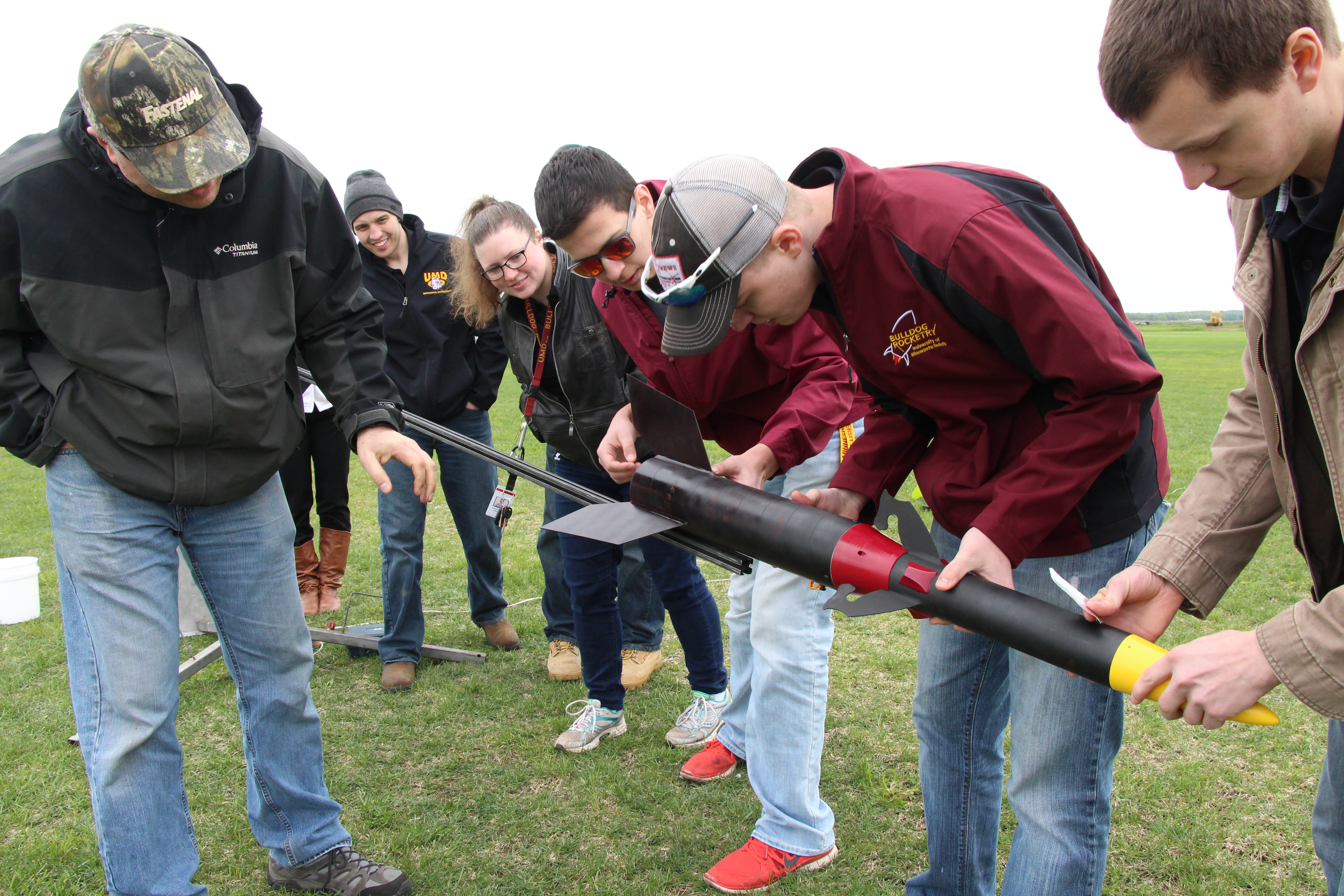 Members of the UMD Bulldog Rocketry Club standing and bending over looking at a rocket.